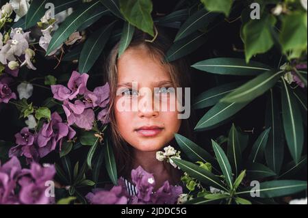 ritratto faccia di capretto bella candido ragazza di otto anni con occhi verdi marroni sullo sfondo di piante verdi e fiori rosa durante una somma Foto Stock