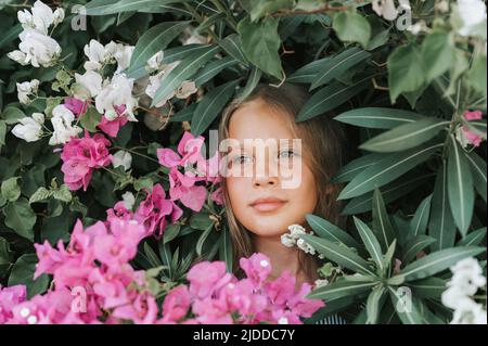 ritratto faccia di capretto bella candido ragazza di otto anni con occhi verdi marroni sullo sfondo di piante verdi e fiori rosa durante una somma Foto Stock