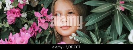ritratto faccia di capretto bella candido ragazza di otto anni con gli occhi marroni sullo sfondo di piante verdi e fiori rosa durante un va estivo Foto Stock