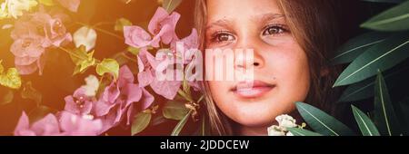 ritratto faccia di bella capretto candido ragazza di otto anni su sfondo di piante verdi e fiori rosa durante una vacanza estiva viaggio. g Foto Stock