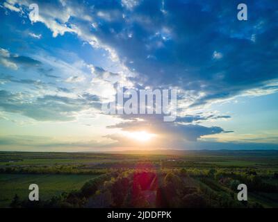 Cielo limpido multicolore senza confini, con nuvole bianche e possenti e un sole splendente dorato, su campi coltivati e allevamenti di bestiame verdi Foto Stock