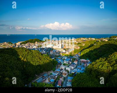 Vista aerea di un piccolo villaggio costiero immerso nella valle tra colline boscose Foto Stock