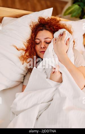 Ragazza pigra rossa nel letto. Una ragazza pigra zenzero che si trova nel suo letto al mattino, coprendo la testa con un lenzuolo, e non vogliono alzarsi. Foto Stock