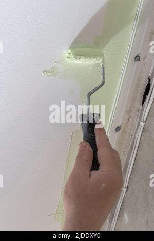 Una mano dell'uomo dipinge una parete con un rullo di vernice, telaio verticale. Costruttore che dipinge un muro in verde. Pittore che dipinge un muro con rullo di vernice. Riparare da Foto Stock