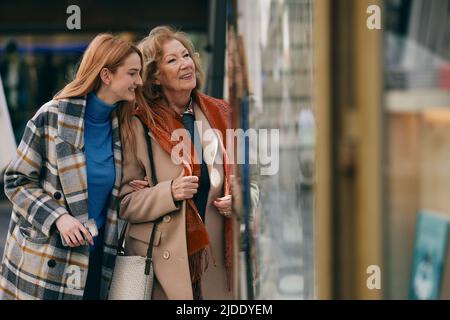 Nonna e nonna adolescente si divertono mentre si fa shopping e si guarda attraverso la vetrina del negozio. Foto Stock