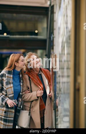 Nonna e nonna adolescente si divertono mentre si fa shopping e si guarda attraverso la vetrina del negozio. Foto Stock