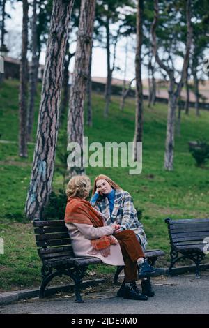 Una nonna ride e si diverte con la nipote adolescente mentre si siede sul banco del parco. Foto Stock