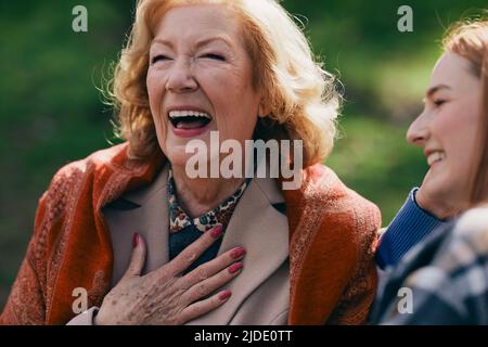 Una nonna ride e si diverte con la nipote adolescente mentre si siede sul banco del parco. Foto Stock