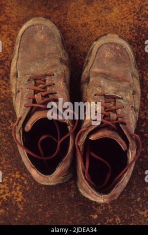 Coppia di stivali da lavoro o da passeggio marroni ben indossati in piedi su lamiera di metallo arrugginita Foto Stock