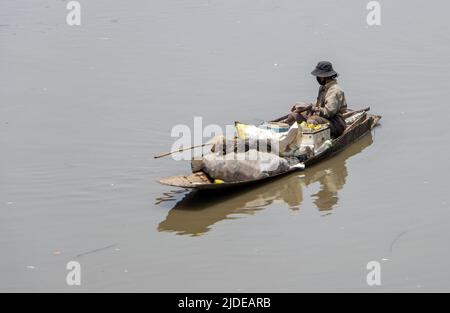 Un povero uomo galleggia su una vecchia barca piena di materiali riciclati Foto Stock