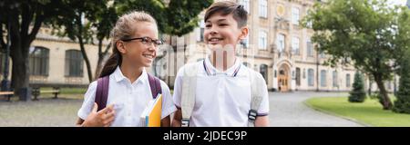 Ragazzi interrazziali positivi con zaini e libri di copia che camminano all'aperto, banner Foto Stock