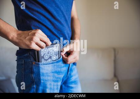 Giovane uomo irriconoscibile che mette il suo ebook nella sua tasca pantaloni, pocketbook Foto Stock