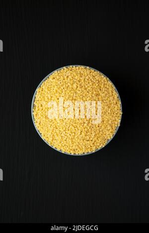 Pasta di Stelline biologica cruda in una ciotola su sfondo nero, vista dall'alto. Disposizione piatta, sovratesta, dall'alto. Foto Stock