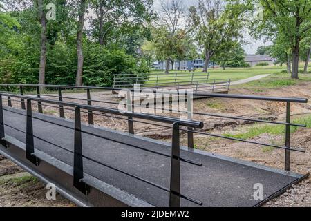 Nuovo ponte di metallo nero su un ruscello, vecchio ponte rimosso e temporaneamente posto sul prato accanto a un sentiero sullo sfondo, alberi verdi in un pub Foto Stock