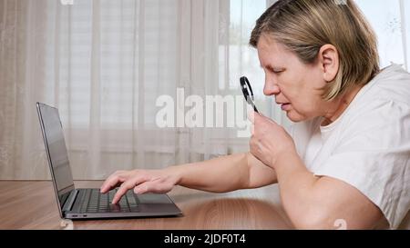 La vecchia donna utilizza la lente d'ingrandimento per digitare sulla tastiera Foto Stock