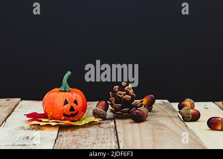 Zucca di Halloween su foglie che sono in cima ad alcuni assi di legno dove c'è anche un cono di pino e ghiande. Lo sfondo è scuro. Foto Stock