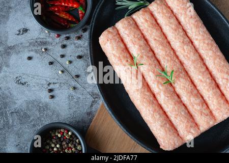 Salsicce fatte in casa crude in una padella su sfondo scuro con spezie. Foto Stock