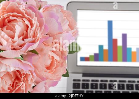 Primo piano peonie rosa e notebook con grafici. Fiori e computer. Foto Stock