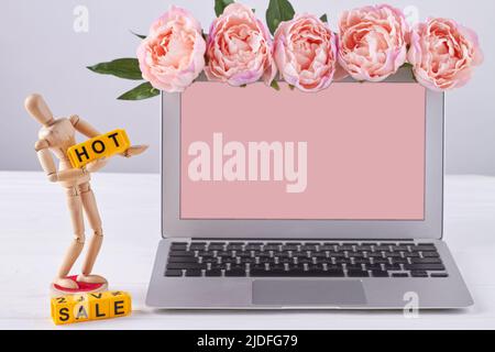 Notebook con schermo rosa per spazio di copia. Concetto di vendita a caldo. Manichino in legno con parole gialle. Foto Stock