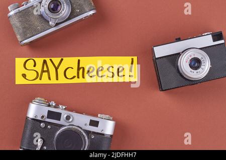 Vista dall'alto tre fotocamere retrò su sfondo rosso. Dite la grafia del formaggio su carta gialla. Foto Stock