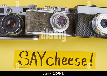 Tre vecchi camer foto retrò su sfondo giallo. Dite la scrittura a mano del formaggio. Foto Stock