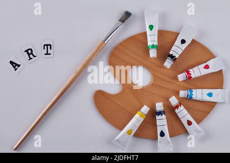 Pennello e tavolozza di legno pulito su sfondo bianco. Pennello per pittura ad olio e tubi colorati. Vista dall'alto concetto artistico. Foto Stock