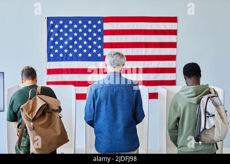 Vista posteriore a tre persone diverse che votano in fila alle cabine contro la bandiera americana, spazio copia Foto Stock