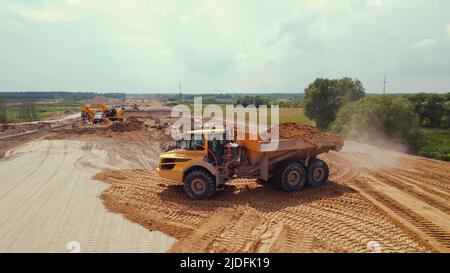 Un autocarro con cassone ribaltabile sporco di colore giallo pieno di un cumulo di sabbia in piedi in un cantiere stradale. Altre macchine industriali in background. Foto di alta qualità Foto Stock