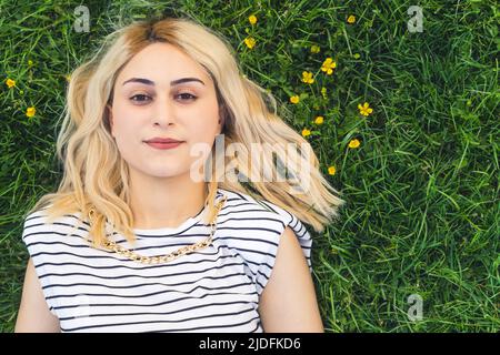 Primo piano medio di una ragazza caucasica bionda adagiata sull'erba verde. Foto di alta qualità Foto Stock