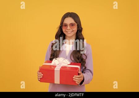 capretto allegro alla moda in occhiali da sole e vestito tenere scatola regalo su sfondo giallo, shopping Foto Stock