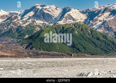 Dischantment Bay, Alaska, USA - 21 luglio 2011: Catena montuosa coperta di neve, alcuni verdi fianchi boschiti vicino al litorale con acqua dell'oceano coperta da fl Foto Stock