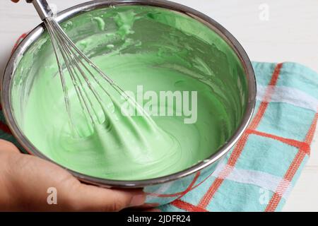 Mescolare la batteria verde con la frusta sul recipiente in acciaio inox. La mano della donna tiene la ciotola, cucinando o cucinando processo Foto Stock