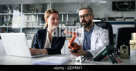 Ingegneri robotici che lavorano su computer portatili e desingendo un moderno braccio robotico in laboratorio. Foto Stock