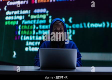 Donna hacker anonima Hooded dal computer nella stanza buia di notte, concetto di ciberwar. Foto Stock