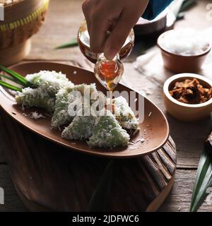 Versare lo zucchero di palma su Lupis, spuntino tradizionale indonesiano a base di riso sticky, avvolto con foglie di Banana, Triangolo di forma servito con zucchero di palma liquido Foto Stock