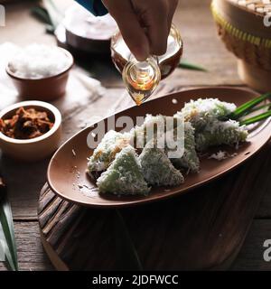 Versare lo zucchero di palma su Lupis, spuntino tradizionale indonesiano a base di riso sticky, avvolto con foglie di Banana, Triangolo di forma servito con zucchero di palma liquido Foto Stock