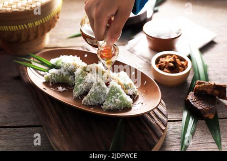 Versare lo zucchero di palma su Lupis, spuntino tradizionale indonesiano a base di riso sticky, avvolto con foglie di Banana, Triangolo di forma servito con zucchero di palma liquido Foto Stock