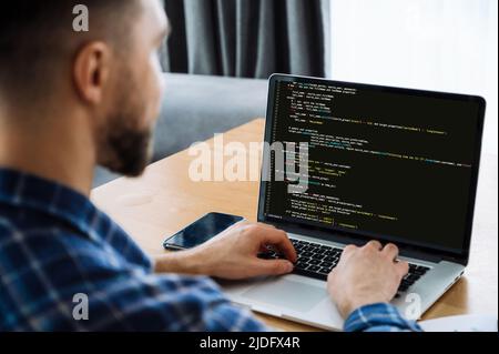 Sviluppo di tecnologie di codifica, CONCETTO IT. Vista sulle spalle di un esperto IT maschile a un computer portatile con codice di programmazione sullo schermo. Programmatore maschio intelligente che lavora su una nuova applicazione software Foto Stock