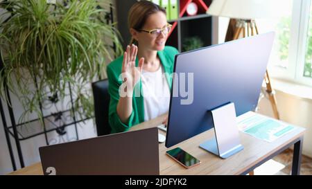 Donna d'affari che ha una videoconferenza e salutando con mano Foto Stock