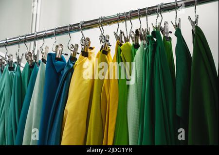 Campioni di tessuto verde giallo e blu appendono sulla barra del rack Foto Stock
