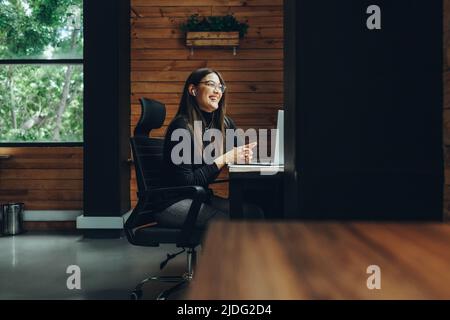 Un'imprenditrice sorridente che ha una riunione virtuale in un moderno spazio di co-working. Felice giovane donna d'affari che comunica con il suo socio di affari Foto Stock