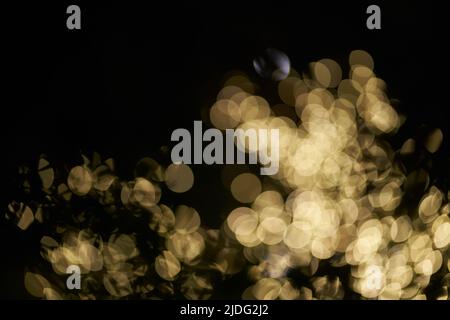 Luci bokeh sfocate e luminose evidenziate su sfondo nero. Sfondo dorato luminoso con luci gialle. Bokeh overlay per il tuo design. Foto di alta qualità Foto Stock