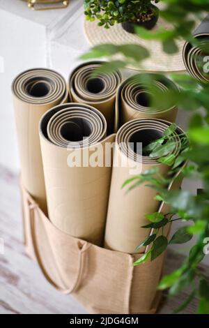 Diversi tappetini in gomma arrotolati per yoga o fitness in colore beige su un pavimento in legno in uno studio. Foto Stock