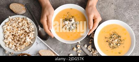 Mani femminili con gustosa zuppa di popcorn in ciotole su sfondo grunge Foto Stock