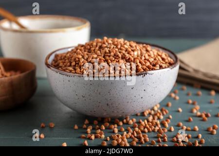 Ciotola con grani di grano saraceno su tavola di legno di colore Foto Stock