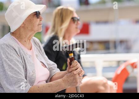 Donna anziana con canna seduta su panca Foto Stock