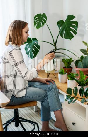 Donna spruzzando casalinga a casa, si preoccupa delle sue piante. Fiorista si prende cura di fiori domestici, versare liquido, fertilizzare, arricchire terreno asciutto, orticoltura, concetto di giardinaggio. Foto Stock