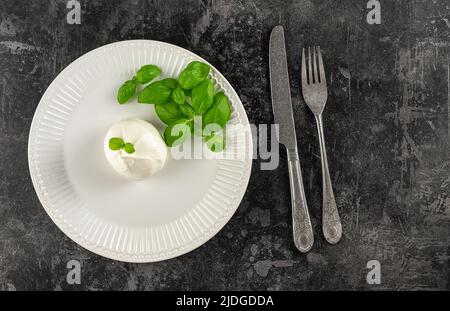 Servizio minimalistico. Burrata italiana mozzarella fresca con una sorpresa interna, il centro è ripieno di panna con basilico verde. Foto Stock