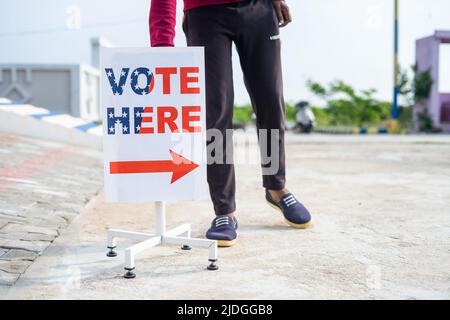 L'uomo che mette il voto qui segno direzione bordo vicino al banco di votazione - concetto di responsabilità, voto o giorno di elezione e la democrazia Foto Stock