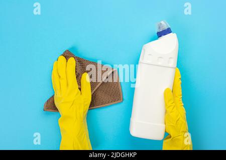 Le mani di una casalinga in guanti protettivi di gomma gialli tengono una bottiglia di prodotti chimici domestici e uno straccio. Detergente per varie superfici nel kitc Foto Stock